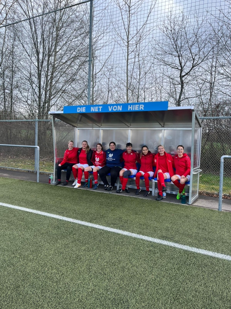 Spielerinnen vol VfL Kaltebtzl sitzen im Unterstand mit der Aufschrift "Die net von hier" 